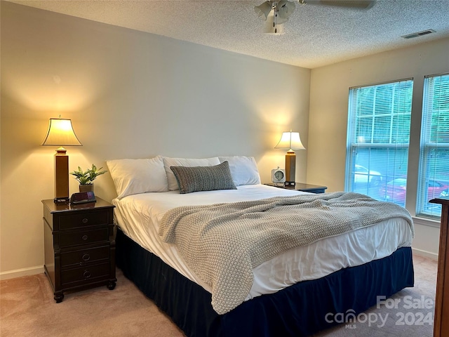 bedroom with ceiling fan, light colored carpet, a textured ceiling, and multiple windows