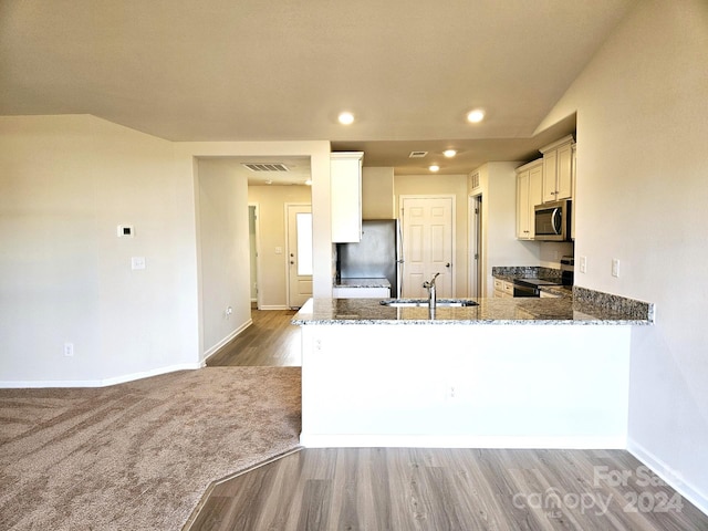 kitchen featuring kitchen peninsula, appliances with stainless steel finishes, dark stone counters, and sink