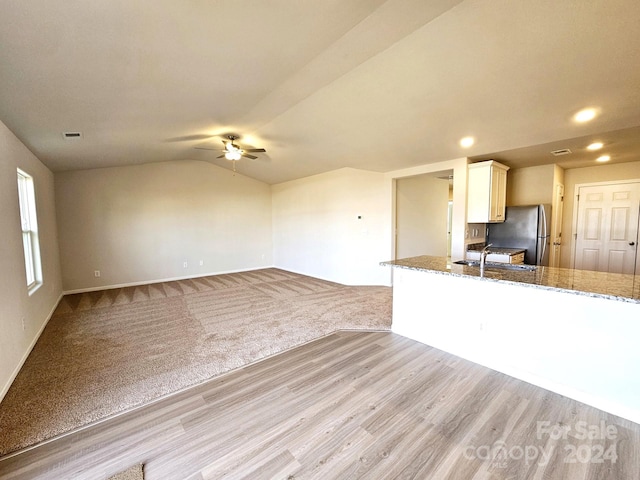 kitchen featuring stone counters, vaulted ceiling, stainless steel fridge, light colored carpet, and white cabinetry