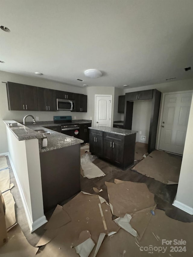 kitchen with kitchen peninsula, black range with electric stovetop, dark stone counters, and sink