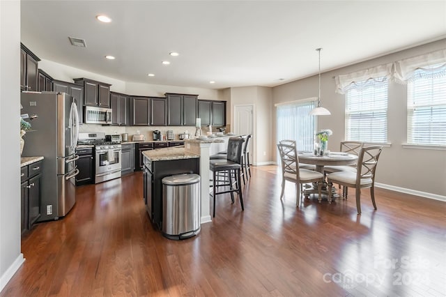 kitchen featuring a kitchen bar, appliances with stainless steel finishes, dark wood-type flooring, pendant lighting, and a center island