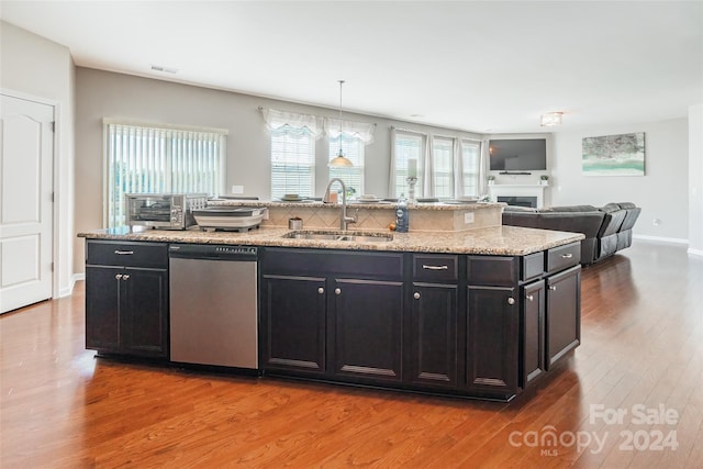 kitchen featuring pendant lighting, hardwood / wood-style floors, a kitchen island with sink, sink, and stainless steel dishwasher