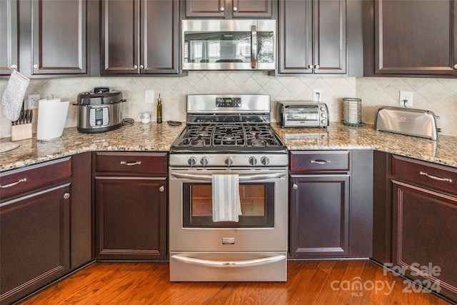 kitchen featuring dark brown cabinetry, dark wood-type flooring, light stone counters, backsplash, and appliances with stainless steel finishes