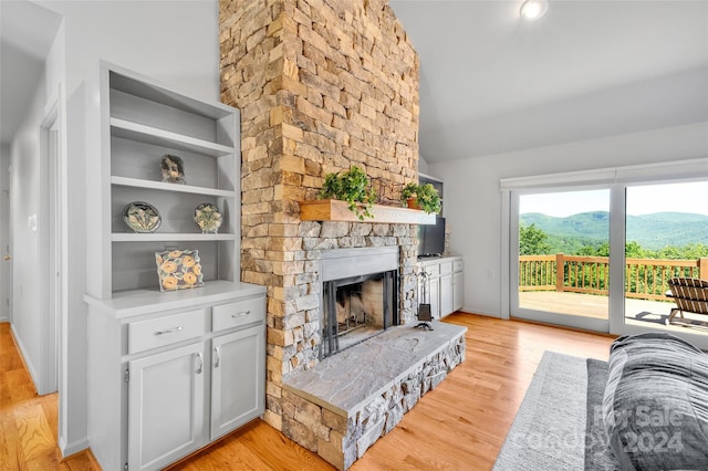 living room featuring built in shelves, light wood-type flooring, a fireplace, and vaulted ceiling