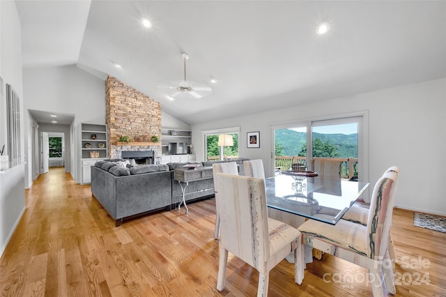 dining area with lofted ceiling, a stone fireplace, built in shelves, ceiling fan, and light hardwood / wood-style floors