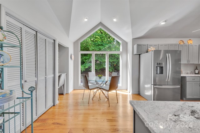 kitchen with stainless steel refrigerator with ice dispenser, vaulted ceiling, gray cabinets, light stone countertops, and light hardwood / wood-style floors