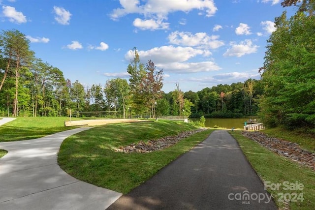 view of property's community featuring a wooded view, a lawn, volleyball court, and a water view