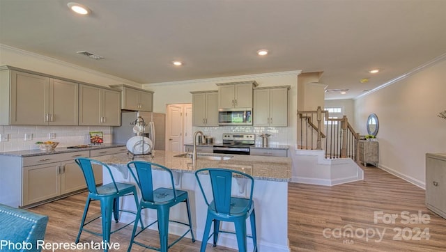 kitchen with sink, an island with sink, light hardwood / wood-style floors, appliances with stainless steel finishes, and ornamental molding