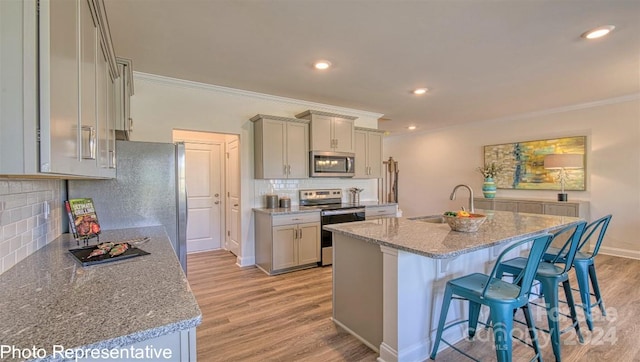 kitchen with light stone countertops, appliances with stainless steel finishes, light wood-type flooring, ornamental molding, and sink