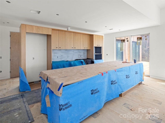 kitchen featuring light brown cabinetry, backsplash, a kitchen island, and light wood-style flooring