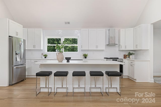 kitchen with a center island, wall chimney range hood, stainless steel fridge with ice dispenser, a breakfast bar area, and white cabinets