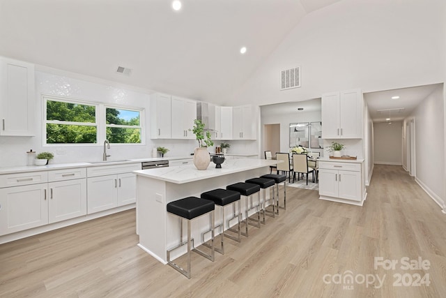 kitchen with a breakfast bar, a center island, high vaulted ceiling, sink, and white cabinetry