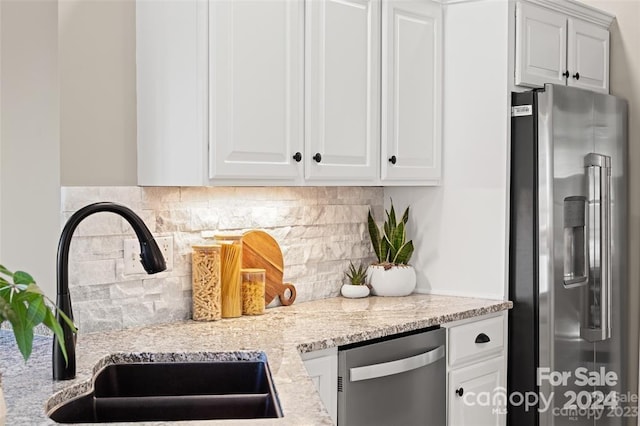 kitchen with backsplash, sink, light stone countertops, white cabinetry, and stainless steel appliances