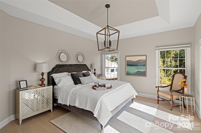 bedroom with a tray ceiling, multiple windows, light hardwood / wood-style flooring, and a chandelier