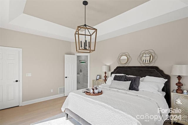 bedroom featuring connected bathroom, a notable chandelier, and light wood-type flooring