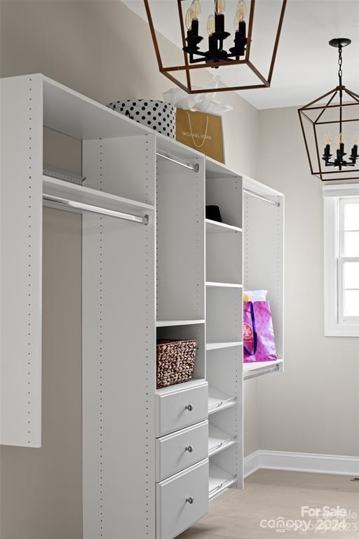 walk in closet with light hardwood / wood-style flooring and a chandelier