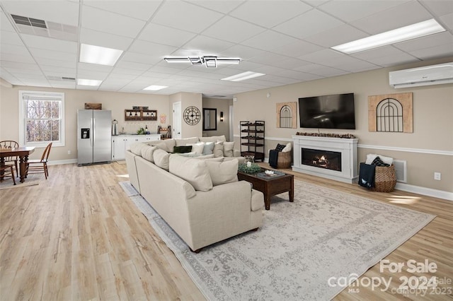 living room with an AC wall unit, a drop ceiling, and light hardwood / wood-style floors