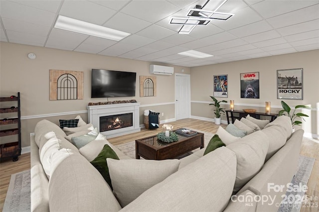 living room with light wood-type flooring, a wall unit AC, and a drop ceiling