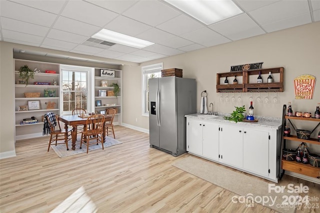 kitchen with sink, a drop ceiling, stainless steel fridge with ice dispenser, light hardwood / wood-style floors, and white cabinets