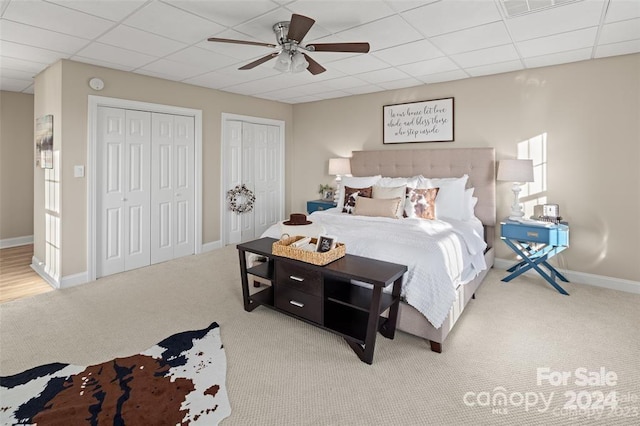 carpeted bedroom featuring a paneled ceiling, ceiling fan, and two closets