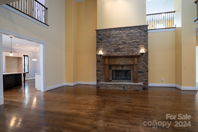 unfurnished living room featuring a towering ceiling, dark wood-type flooring, a stone fireplace, and crown molding