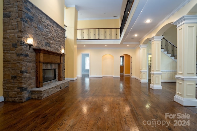 unfurnished living room featuring a high ceiling, crown molding, ornate columns, a fireplace, and dark hardwood / wood-style flooring