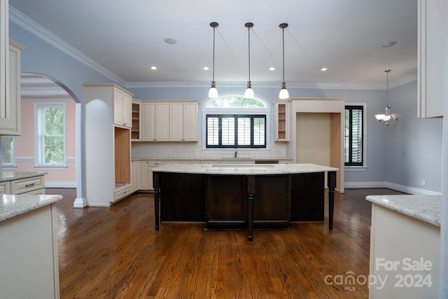 kitchen featuring pendant lighting, backsplash, ornamental molding, a kitchen island, and light stone counters