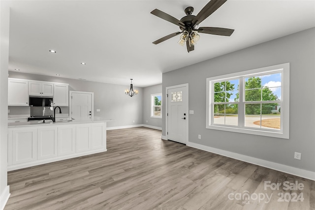 kitchen with white cabinetry, hanging light fixtures, ceiling fan with notable chandelier, and light hardwood / wood-style floors