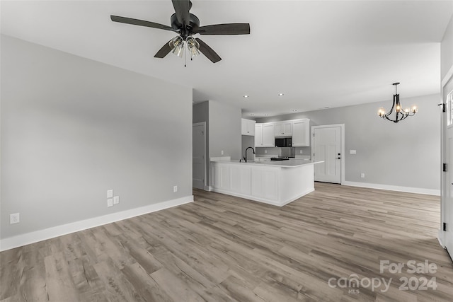 unfurnished living room with ceiling fan with notable chandelier, light wood-type flooring, and sink