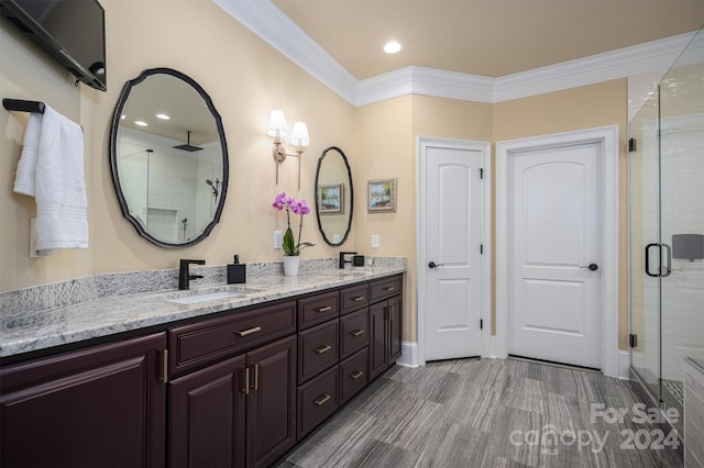 bathroom with double sink vanity, a shower with door, and ornamental molding