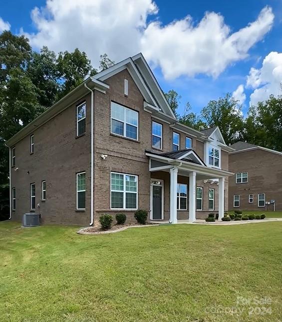 rear view of property with a lawn, brick siding, and cooling unit