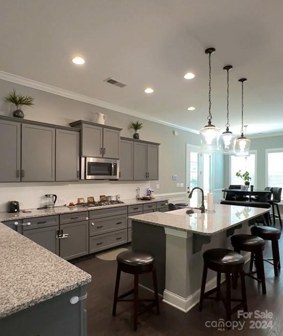 kitchen with appliances with stainless steel finishes, an island with sink, light stone countertops, gray cabinets, and a kitchen bar