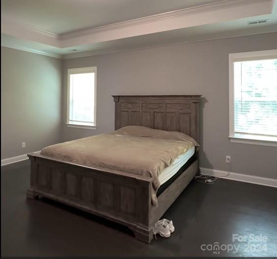 bedroom with a raised ceiling, crown molding, baseboards, and visible vents