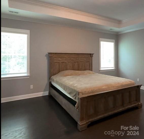 bedroom featuring a raised ceiling, crown molding, dark wood-type flooring, and multiple windows