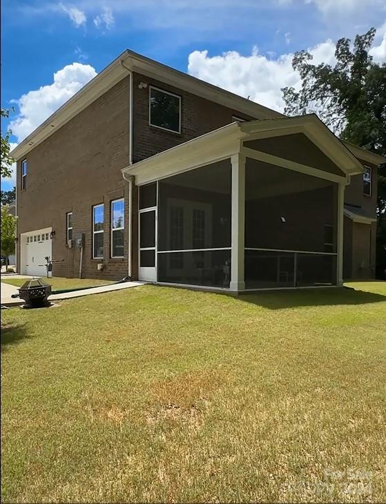 back of property featuring a garage, a sunroom, and a lawn