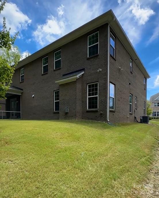 rear view of house with a lawn, central AC, and brick siding
