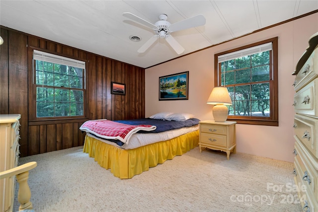 bedroom featuring carpet flooring, ceiling fan, wood walls, and multiple windows