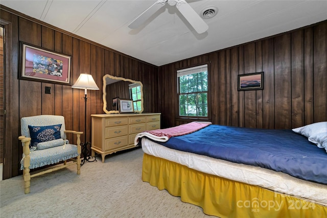 bedroom with ceiling fan, wooden walls, and light colored carpet