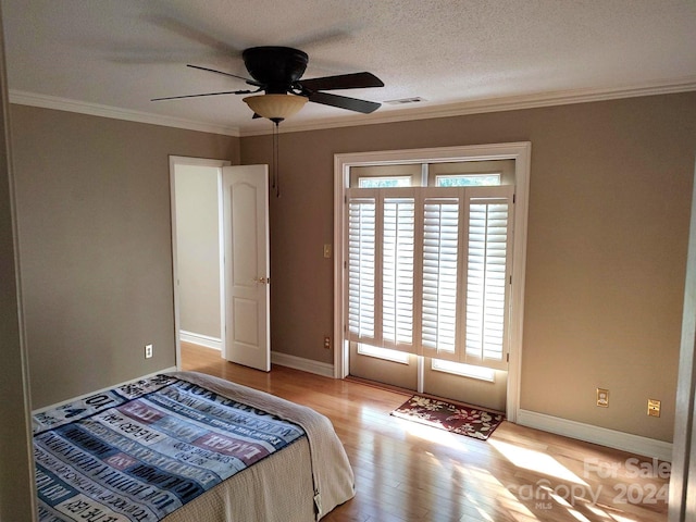 bedroom with ceiling fan, a textured ceiling, ornamental molding, and light hardwood / wood-style floors