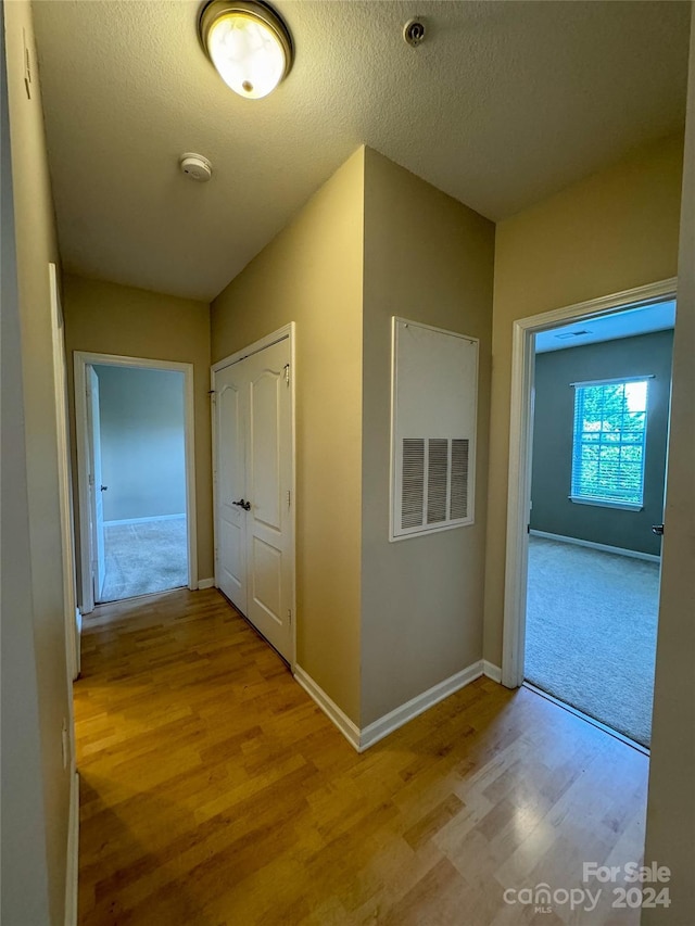 hallway featuring light wood-type flooring and a textured ceiling