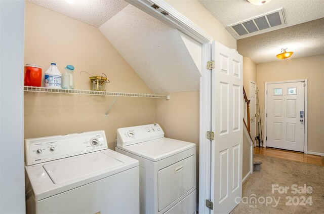 clothes washing area featuring light carpet, washer and dryer, and a textured ceiling