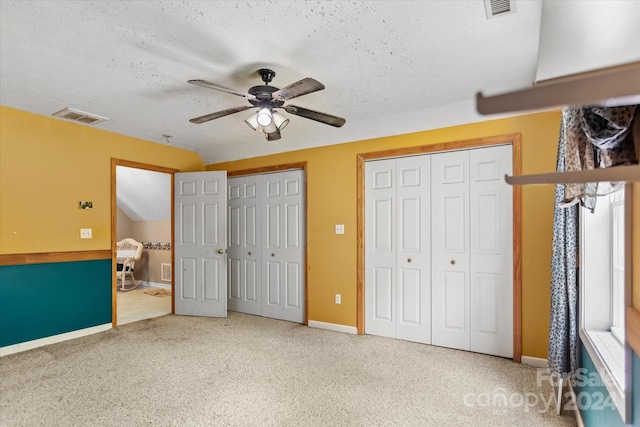 unfurnished bedroom with carpet flooring, a textured ceiling, two closets, and ceiling fan