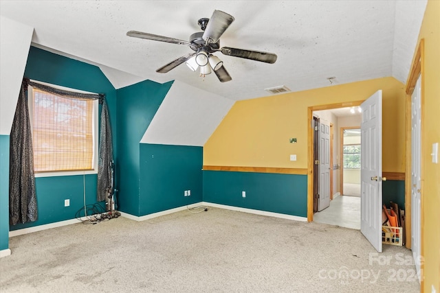 additional living space with ceiling fan, a textured ceiling, light carpet, and lofted ceiling