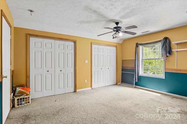 unfurnished bedroom with ceiling fan, two closets, a textured ceiling, and carpet floors