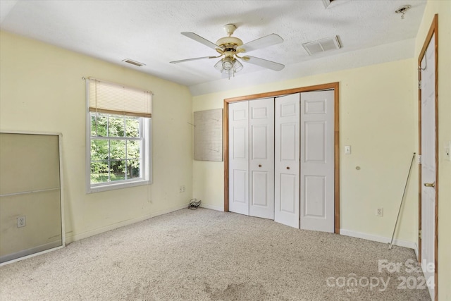 unfurnished bedroom with a closet, ceiling fan, light colored carpet, and a textured ceiling