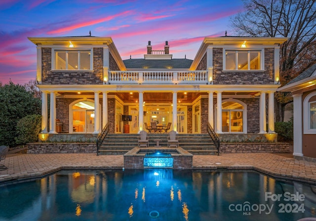 back house at dusk featuring a patio area and a pool with hot tub