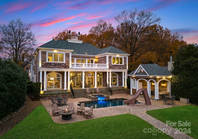 back house at dusk with a yard, a balcony, a fire pit, and a patio area