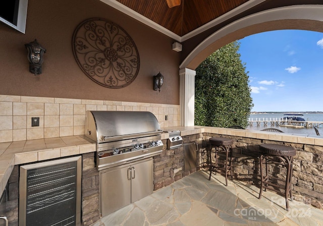 view of patio / terrace featuring an outdoor kitchen, exterior bar, a water view, wine cooler, and a grill