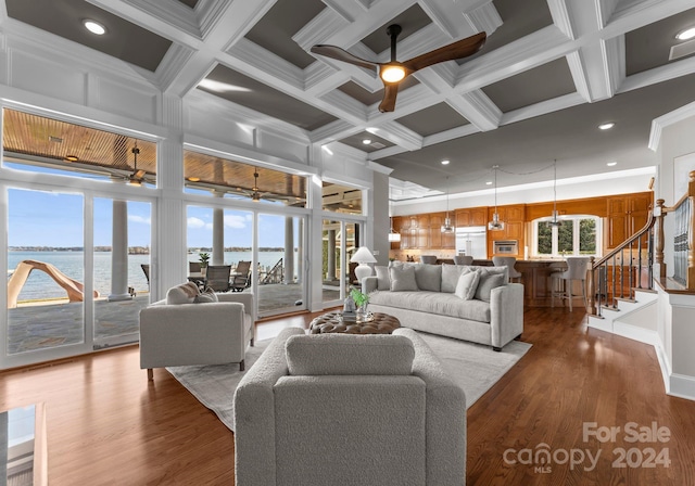 living room with a water view, dark wood-type flooring, coffered ceiling, and ornamental molding