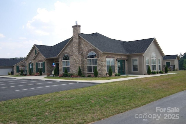 view of front of house with a shingled roof, a front yard, uncovered parking, and a chimney